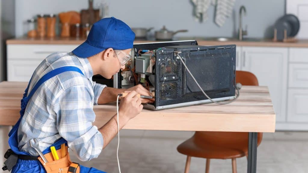 worker repairing microwave oven in kitchen 1024x576